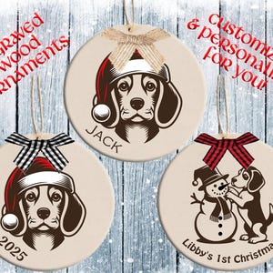 May include: Three round, cream-colored Christmas ornaments with dog illustrations wearing Santa hats. One ornament says "JACK", another says "2025", and the third says "Libby's 1st Christmas". Each ornament has a decorative bow and a string for hanging.