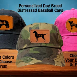 May include: Three personalized distressed baseball caps with different dog breeds and names. The caps are in black, camouflage, and pink. The text on the caps reads "Jack", "Lucy", and "Rowdy".