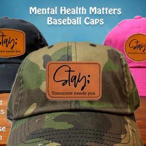 May include: Three baseball caps with the text "Stay; Tomorrow needs you" on a leather patch. The caps are in black, camouflage, and pink. The image also includes the text "Mental Health Matters Baseball Caps" and "8 Hat Colors To Choose From".