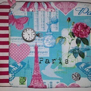 May include: A blue and pink fabric pot holder with a Parisian theme. The fabric features images of the Eiffel Tower, butterflies, roses, a clock, and a perfume bottle. The text "Paris" is printed on the fabric.