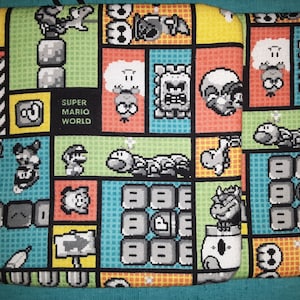 May include: A colorful fabric pouch with a Super Mario World theme. The pouch features various characters and objects from the game, including Mario, Luigi, Goombas, and Koopa Troopas. The pouch is made of a soft, durable fabric and is perfect for storing small items.