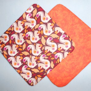 Könnte beinhalten: Zwei Topfhandschuhe in Braun und Orange mit einem Muster aus Eichhörnchen und Blättern. Die Topfhandschuhe sind aus Stoff und haben eine gesteppte Textur.