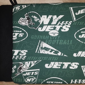 May include: A green and white NY Jets pot holder with a black pot holder. The green pot holder has a repeating pattern of the NY Jets logo, football helmets, and the words "JETS" and "Gotham City Football".
