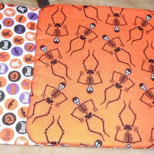 May include: Two Halloween-themed pot holders. One features a pattern of orange, purple, and black circles with skulls, bats, and the word "Boo!". The other has a repeating pattern of brown skeletons on an orange background.