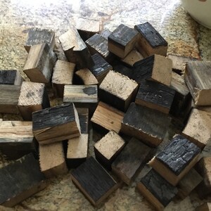 May include: A pile of small, charred wood cubes, some with a natural wood color, others with a dark brown char. The cubes are likely for smoking food.