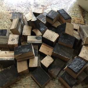 May include: A pile of small, charred wood cubes, some with a darker brown color, perfect for smoking meats or adding a smoky flavor to food.
