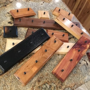 May include: A collection of wooden display stands with black metal pegs. The stands are in various wood tones, including natural, stained, and black.