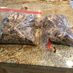 May include: Two clear plastic bags filled with brown wood chips. The bags are on a brown and black speckled countertop.