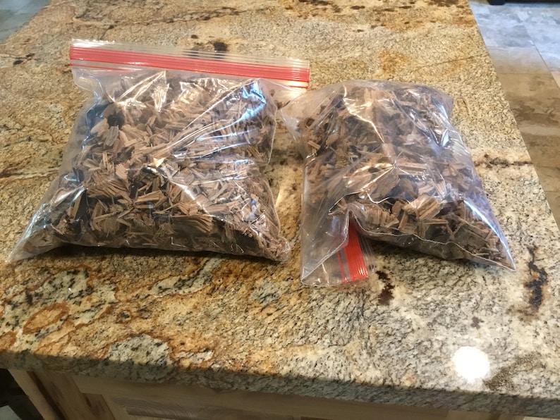 May include: Two clear plastic bags filled with brown wood chips. The bags are on a brown and black speckled countertop.