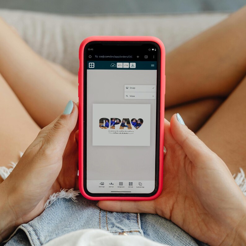 Puede incluir: Un tel&eacute;fono inteligente con una funda rosa brillante muestra una imagen digital con la palabra "OPA" y un s&iacute;mbolo de coraz&oacute;n. La imagen est&aacute; sobre un fondo blanco. El tel&eacute;fono lo sostiene una persona que lleva pantalones cortos de mezclilla.