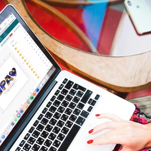 Puede incluir: Un port&aacute;til plateado con teclado negro est&aacute; abierto sobre una mesa de madera. La pantalla muestra una p&aacute;gina web con un collage de fotos. Un smartphone blanco est&aacute; sobre la mesa. Una mano con esmalte de u&ntilde;as rojo utiliza el port&aacute;til.