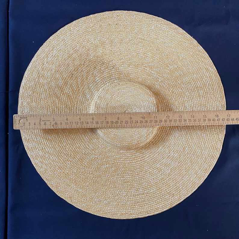 K&ouml;nnte beinhalten: Ein beigefarbener Sonnenhut mit breiter Krempe und kreisf&ouml;rmigem Muster. Der Hut hat einen Krempen-Durchmesser von ca. 43 cm. Der Hut besteht aus gewebtem Material und liegt auf einem dunkelblauen Hintergrund.