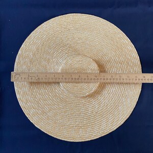 K&ouml;nnte beinhalten: Beigefarbener Strohhut mit breiter Krempe und kreisf&ouml;rmigem Design. Der Hut hat einen Krempen-Durchmesser von etwa 43 cm. Ein Holzlineal liegt zur Messung auf dem Hut.