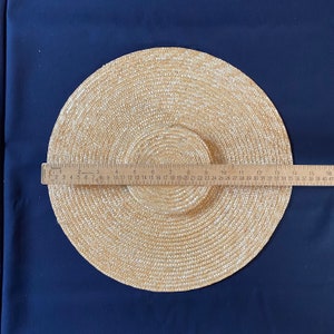 K&ouml;nnte beinhalten: Ein Sonnenhut aus Stroh mit breiter Krempe, etwa 40 cm im Durchmesser, wird vor einem dunkelblauen Hintergrund gezeigt. Der Hut besteht aus gewebtem Stroh und hat eine kreisf&ouml;rmige Krone und Krempe. Ein Lineal liegt zur Messung auf dem Hut.