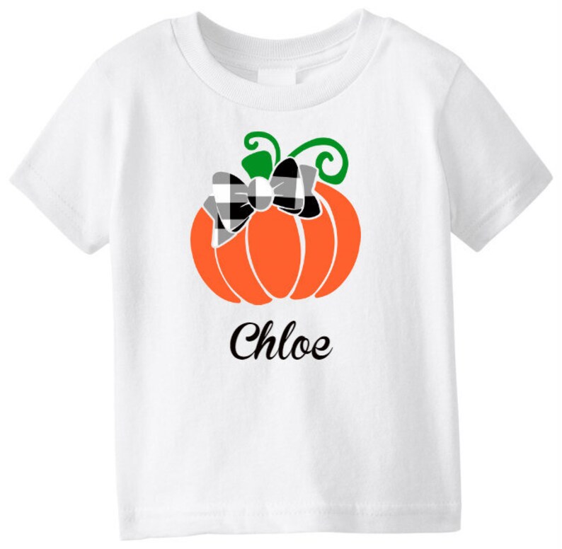 May include: White t-shirt with a black and white checkered bow on an orange pumpkin. The text "Chloe" is printed below the pumpkin.