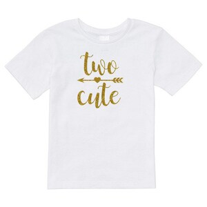 May include: White t-shirt with gold glitter lettering that says "two cute" with an arrow and heart in between the words.