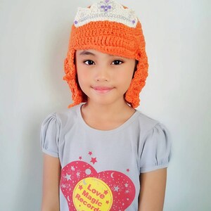 Puede incluir: Una persona joven con un gorro de punto naranja con una corona blanca y una camiseta gris con un corazón rojo y el texto "Love Magic Records".