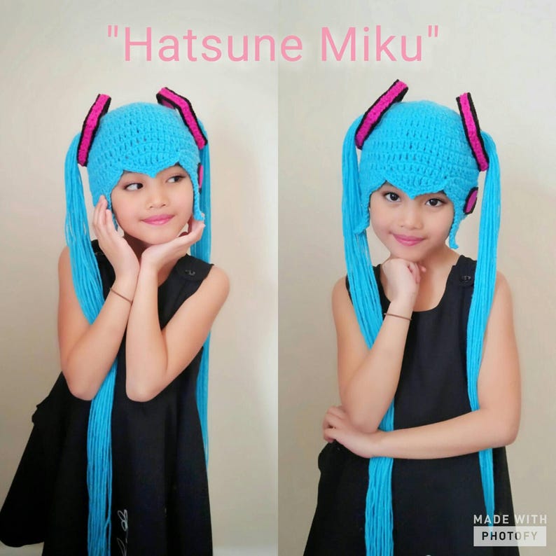 May include: A child wearing a blue and pink crocheted hat with long blue yarn tails. The hat is styled like the character Hatsune Miku. The text "Hatsune Miku" is written above the image.