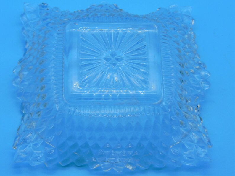 Puede incluir: Un plato cuadrado de vidrio transparente con un patr&oacute;n de diamante elevado alrededor del borde y un patr&oacute;n de estrella en el centro.