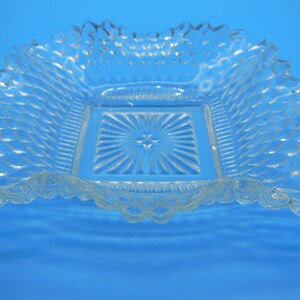 Puede incluir: Un plato de vidrio transparente con un centro cuadrado y un borde festoneado. El plato tiene un patr&oacute;n de diamante en toda su superficie.