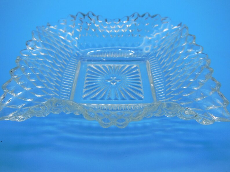 Puede incluir: Un plato de vidrio transparente con un centro cuadrado y un borde festoneado. El plato tiene un patr&oacute;n de diamante en toda su superficie.