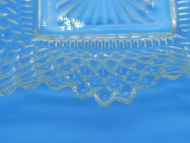 Puede incluir: Primer plano del borde inferior de un plato de vidrio transparente con un patr&oacute;n de diamante. El plato tiene un borde festoneado.
