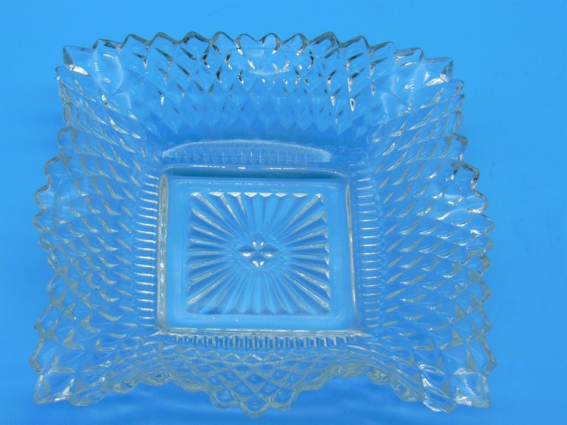Puede incluir: Un plato cuadrado de vidrio transparente con un patr&oacute;n elevado en forma de diamante alrededor del borde y un cuadrado m&aacute;s peque&ntilde;o en el centro con un patr&oacute;n de estrella.
