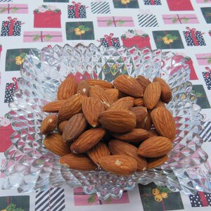 Puede incluir: Un bol de vidrio transparente lleno de almendras. Las almendras son de color marr&oacute;n claro y est&aacute;n dispuestas en un patr&oacute;n aleatorio. El bol est&aacute; sobre una superficie con un patr&oacute;n blanco y rojo.