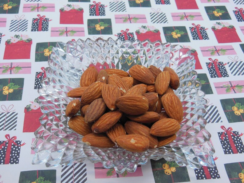 Puede incluir: Un bol de vidrio transparente lleno de almendras. Las almendras son de color marr&oacute;n claro y est&aacute;n dispuestas en un patr&oacute;n aleatorio. El bol est&aacute; sobre una superficie con un patr&oacute;n blanco y rojo.