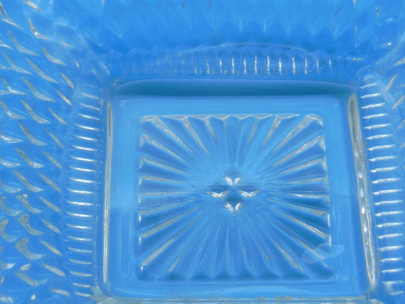 Puede incluir: Un plato de vidrio azul con un patr&oacute;n decorativo en forma de estrella. El plato tiene una forma cuadrada y un borde elevado.