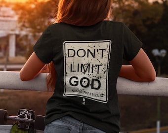 May include: Black t-shirt with a distressed white graphic that reads "DON'T LIMIT GOD" and "NUMBERS 11:23". The shirt is worn by a person leaning on a white railing, with a skateboard visible.
