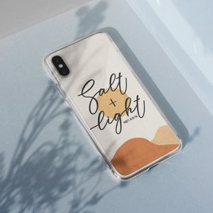 May include: Clear phone case with a cream-colored background featuring the words "Salt + Light" in black script, with a gold circle and brown abstract shapes. The text "MATT. 5:13-16" is below the words.