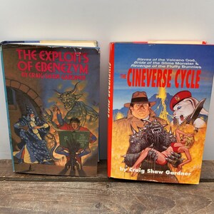 May include: Two paperback fantasy novels with colorful covers. The first book is titled "The Exploits of Ebenezym" by Craig Shaw Gardner. The second book is titled "The Cineverse Cycle" by Craig Shaw Gardner. The covers feature illustrations of fantastical creatures and characters.