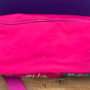 May include: A pink nylon tote bag with a purple zipper and a colorful graphic print on the bottom. The bag has a purple strap.