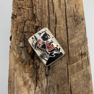 May include: A silver-toned pin with a black and red enamel design of a bear carrying a smaller bear on its back. The bear is walking through a forest scene.