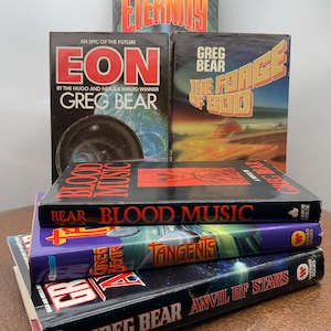 May include: A stack of science fiction books by Greg Bear. Titles include "Eternity", "Eon", "The Forge of God", "Blood Music", "Tangents", and "Anvil of Stars". The books have colorful covers with text and graphic designs.