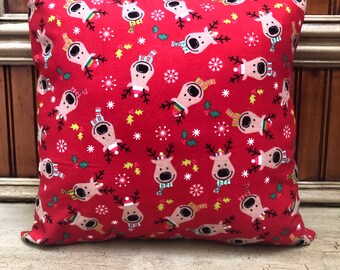May include: Red throw pillow with a festive pattern of reindeer wearing Santa hats and scarves on a white background. The pillow is filled with a soft, comfortable material.