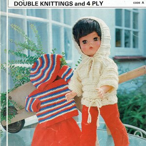 Könnte beinhalten: Eine Puppe trägt ein cremefarbenes Strick-Outfit, bestehend aus einem Kapuzenpullover und einer roten Hose. Ein weiteres Outfit mit rotem Rock und gestreiftem blau-weiß-rotem Oberteil ist ebenfalls abgebildet. Der Text "spunlaine" steht oben.