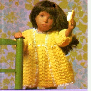May include: A vintage image of a doll wearing a yellow crochet dress with white trim. The doll has dark hair and is holding a small object. The background features a floral pattern in yellow and green.