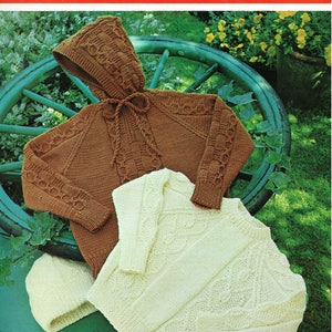 Puede incluir: Dos jerséis de punto, uno marrón con capucha y el otro blanco, con un patrón de punto de cable. Los jerséis están colocados sobre una superficie verde con una rueda de madera detrás. El texto "Broute REGD Double Knitting To fit 61 to 76 cm chest (24 to 30 inch) 778" está impreso sobre un fondo rojo en la parte superior de la imagen.