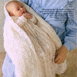 Puede incluir: Una bata de bautizo de bebé de ganchillo blanco y un chal a juego. La bata tiene un corpiño calado y bordes festoneados. El chal es de forma cuadrada. El texto "7915 Baby 3 Ply" está impreso en la esquina superior derecha de la imagen.