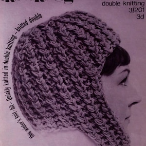 May include: A purple knitted hat with a fold-down flap, called "The Snuggle", made with Courtelle double knitting yarn. The pattern is from Bairnswear and is number 3/201.