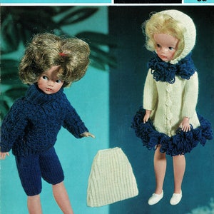 May include: An advertisement for doll clothes. Two dolls are dressed in knitted outfits. One doll wears a navy blue sweater and shorts. The other doll wears a white coat with navy blue trim. A white knitted hat is also shown. The text reads "Majestic 3 ply or Gaiety Nylon 3 ply Dolls Clothes - to fit 12" Doll".