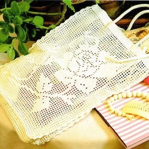 以下が含まれることがあります： 花柄の白いクロシェのトートバッグ。バッグはシングルハンドルで、繊細なオープンステッチで作られています。