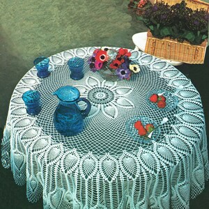 May include: White crocheted table cloth with a delicate lace pattern. The tablecloth is laid on a round table with blue glass cups and a pitcher, and a bowl of red strawberries.