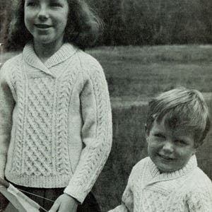 Könnte beinhalten: Zwei Kinder tragen weiße Strickpullover mit Kabelmuster und Kragen. Das Mädchen hält einen weißen Drachen.