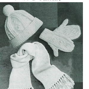 Puede incluir: Conjunto de gorro, bufanda y guantes de punto blanco para niños. El gorro tiene un pompón en la parte superior y la bufanda tiene flecos. "Childrens ARAN Bobble Hat, Scarf & Mittens" está escrito en la imagen.