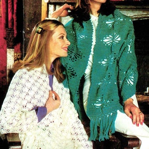 May include: Two women wearing crocheted shawls. The woman on the left is wearing a white shawl with a delicate lace pattern and fringe. The woman on the right is wearing a teal shawl with a floral pattern and fringe.