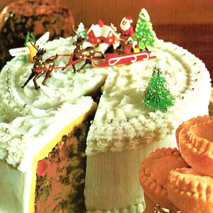 May include: A white frosted cake decorated with a miniature Santa Claus and reindeer pulling a sleigh. The cake is surrounded by small, round pastries.