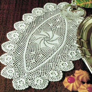 May include: White crocheted oval table runner with a swirling pattern in the center and a scalloped edge.